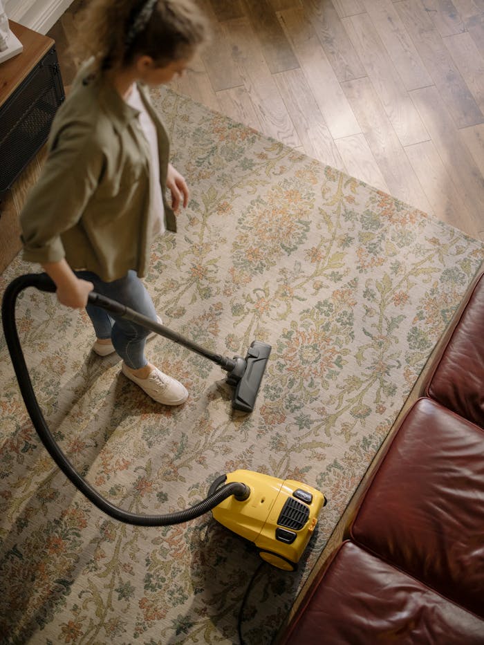 services-01 Overhead view of a woman vacuuming a carpet at home, highlighting cleanliness and housekeeping.