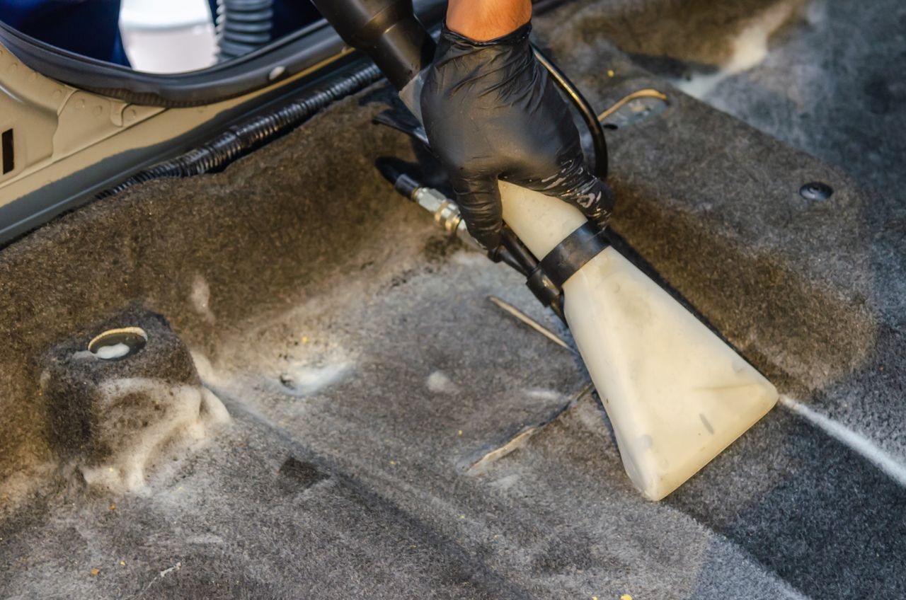 services-03 A hand in a glove using a vacuum to clean a car interior carpet, removing dirt effectively.