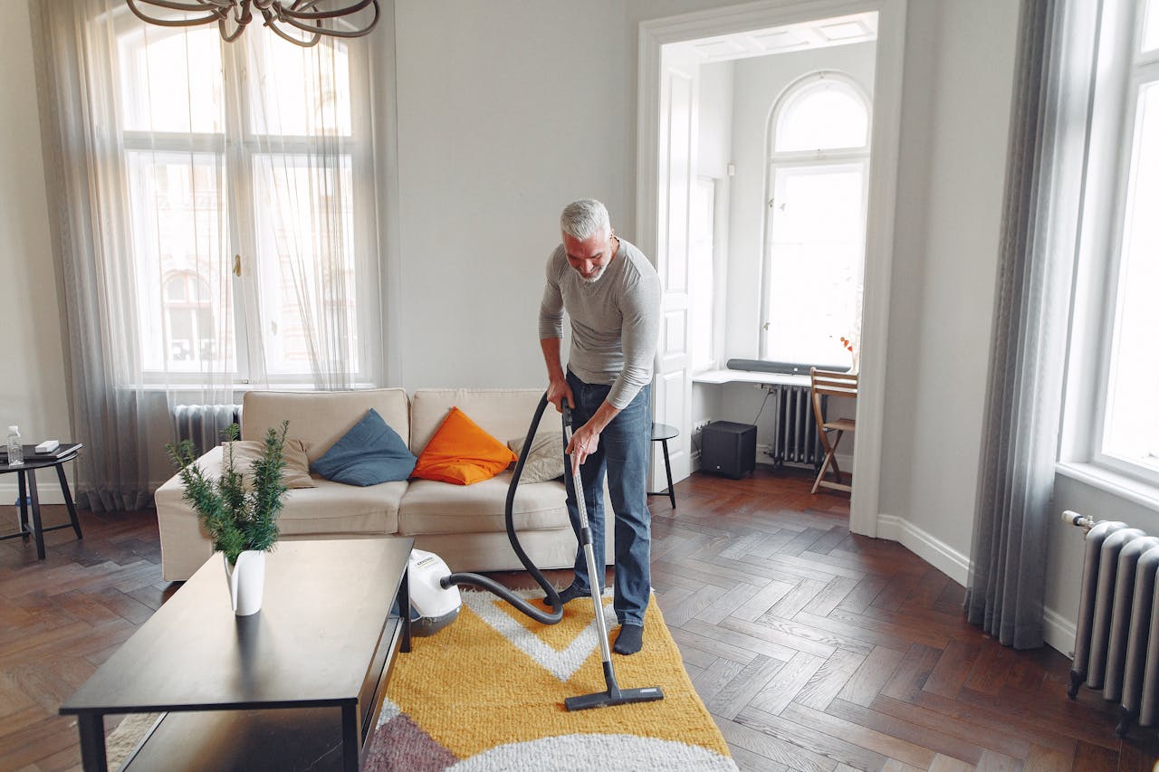 hero-img-02 From above of focused grey haired man with beard vacuum cleaning carpet at home