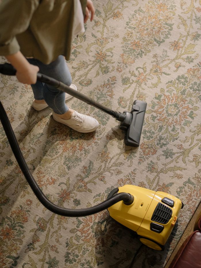 about-01 Person cleaning a floral carpet with a yellow vacuum cleaner indoors.